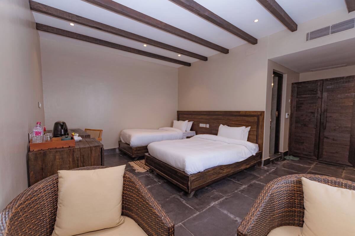 A bedroom with two beds, wicker furniture, a wooden dresser, and a stone floor.