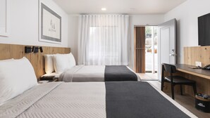 Habitación de hotel con dos camas, un escritorio, una silla, un televisor y una puerta que da a un balcón.