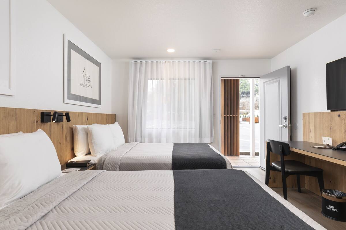 A hotel room with two beds, a desk, a chair, a TV, and a door leading to a balcony.