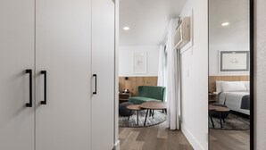 Una habitación de hotel moderna con un espejo grande, un sofá verde, una mesa de centro redonda y una cama con cabecera blanca.