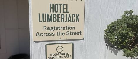 A sign for Sonora Inn Hotel Lumberjack indicating registration across the street and a designated smoking area.