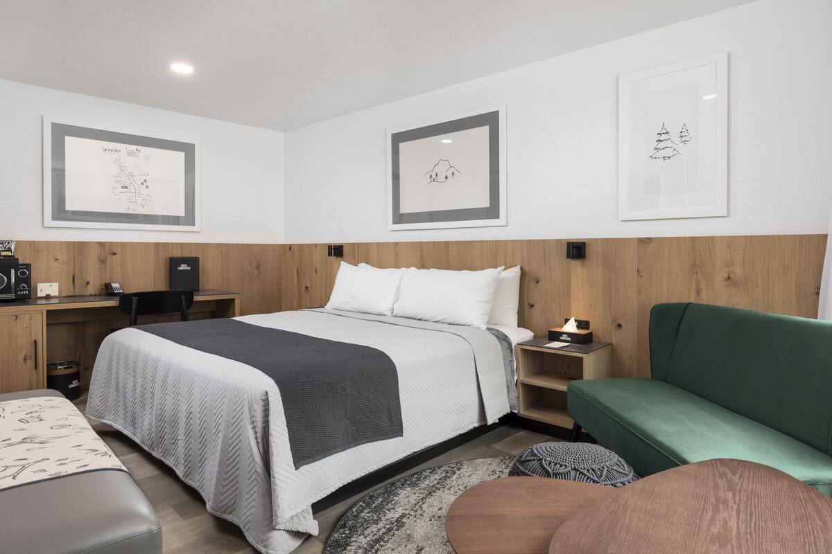 A hotel room with a bed, a desk, a green sofa, and framed pictures on the wall.