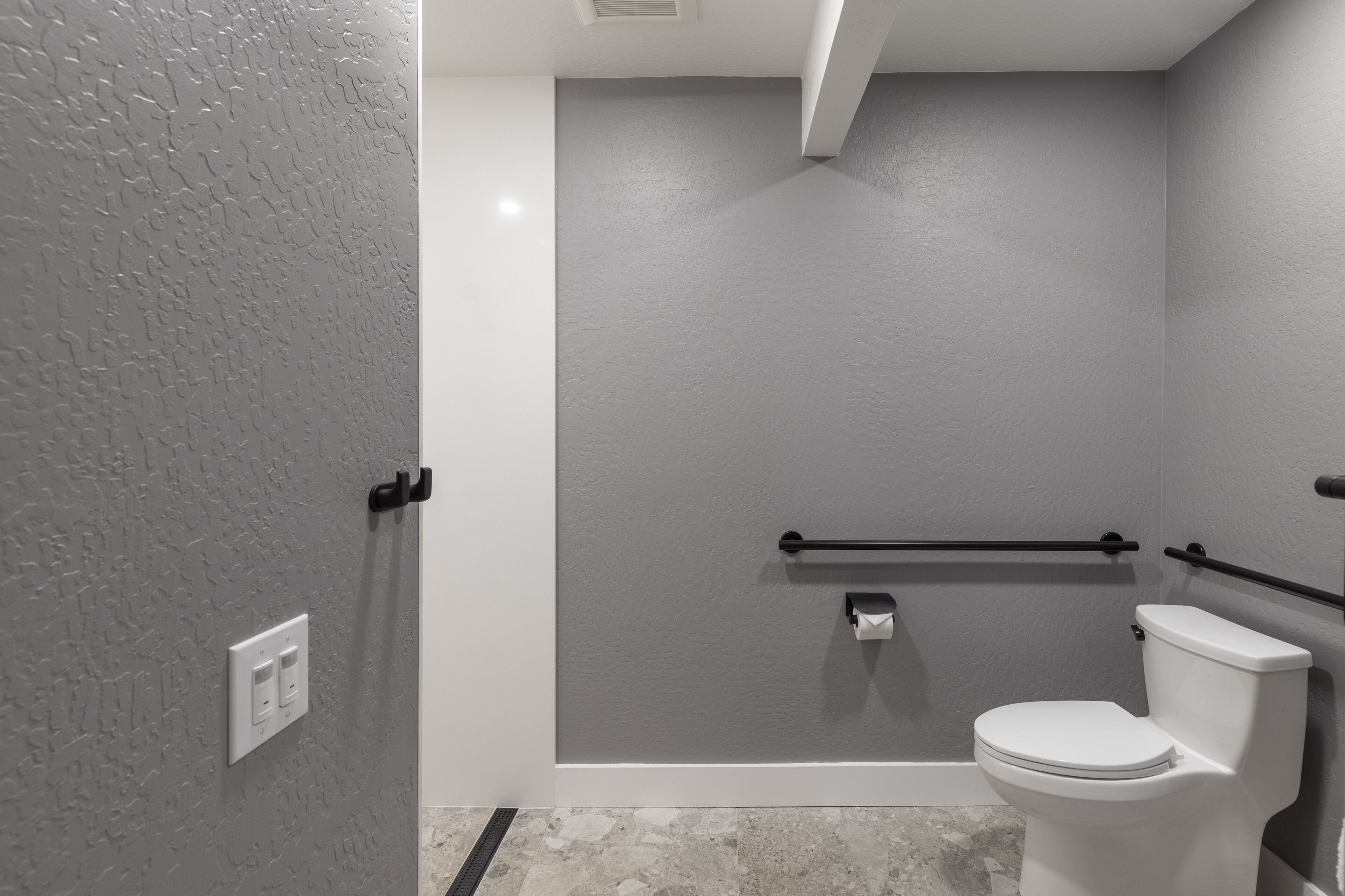 A modern bathroom with a white toilet, a shower area with a glass door, and a handrail.