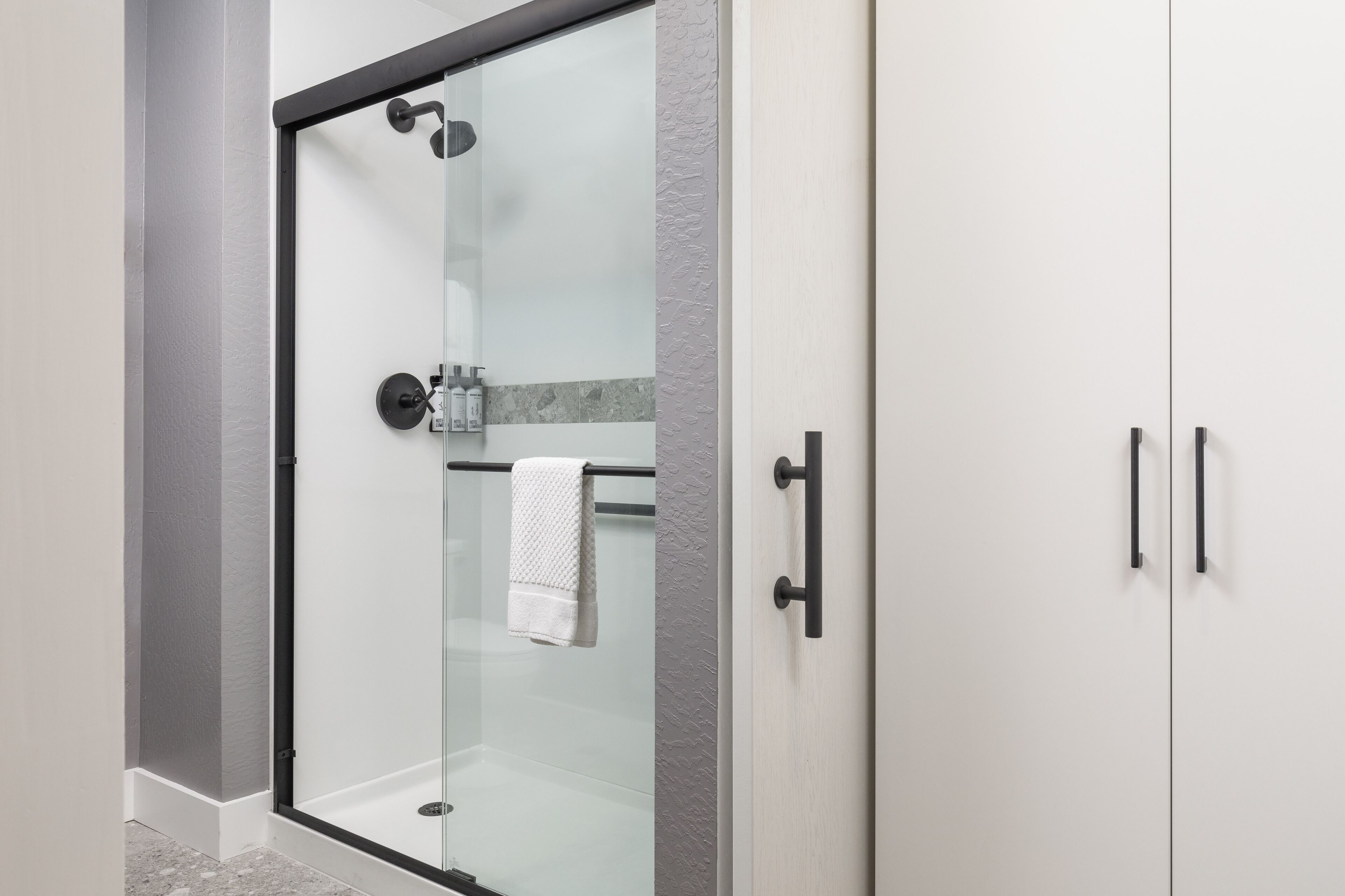 Un baño moderno con ducha envuelta en vidrio, un perchero y un mueble con dos pomos.