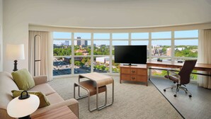 A hotel room with a large window, a flat-screen TV, a desk, a chair, a sofa, and a lamp. - Homewood Suites by Hilton Atlanta Midtown, GA (Atlanta)