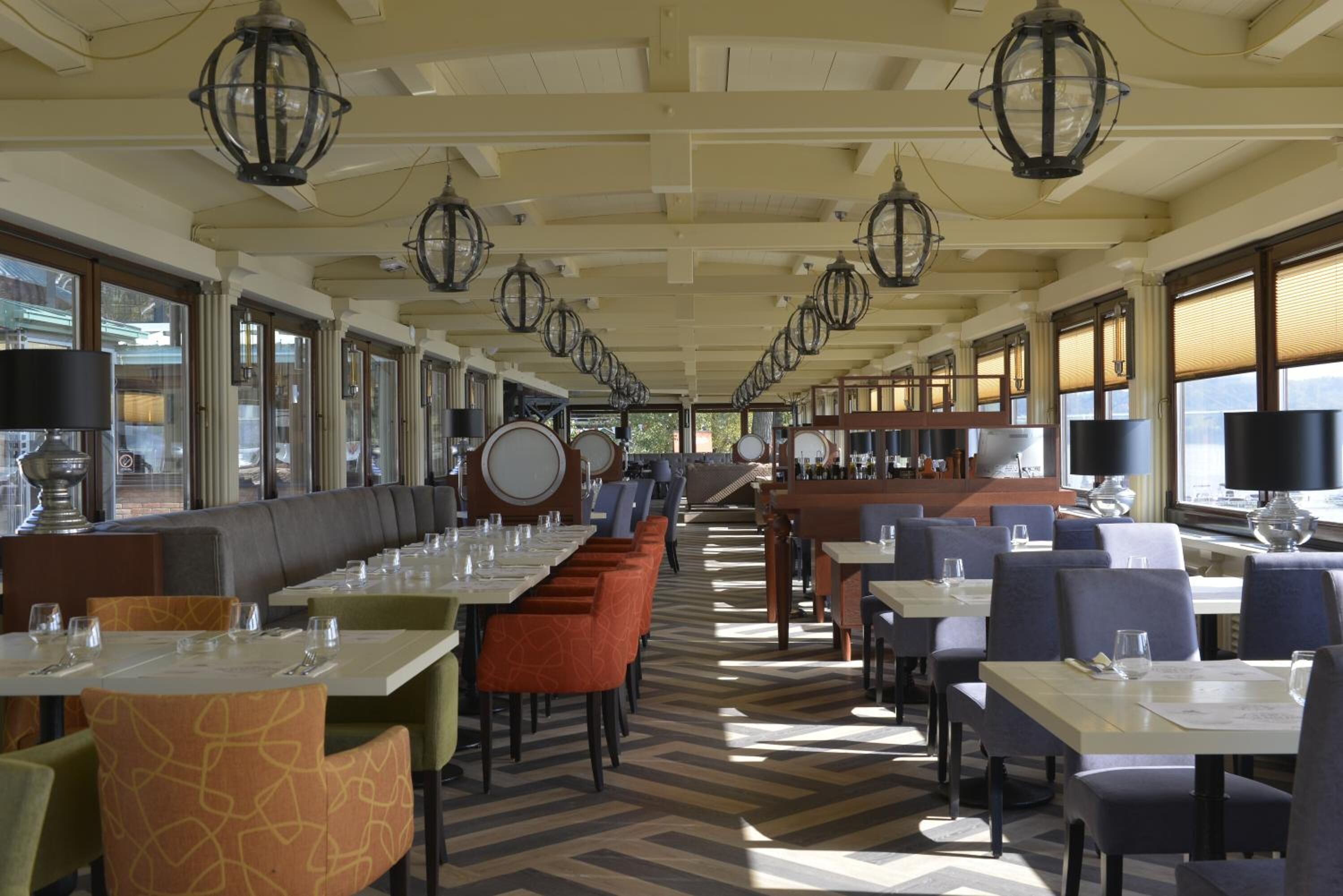 Un restaurante con mesas largas, cabinas, ventanas amplias y lámparas colgantes tipo farol.