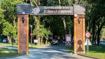 An entrance gate with a sign reading "Turističko naselje Ribarsko ostrvo" and a speed limit sign of 20 km/h.