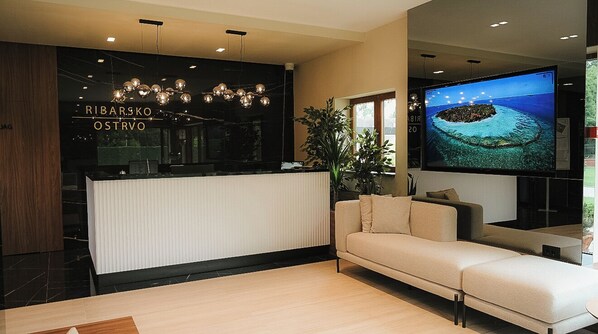 A modern reception area with a black counter, a large flat-screen TV, and a beige sofa.