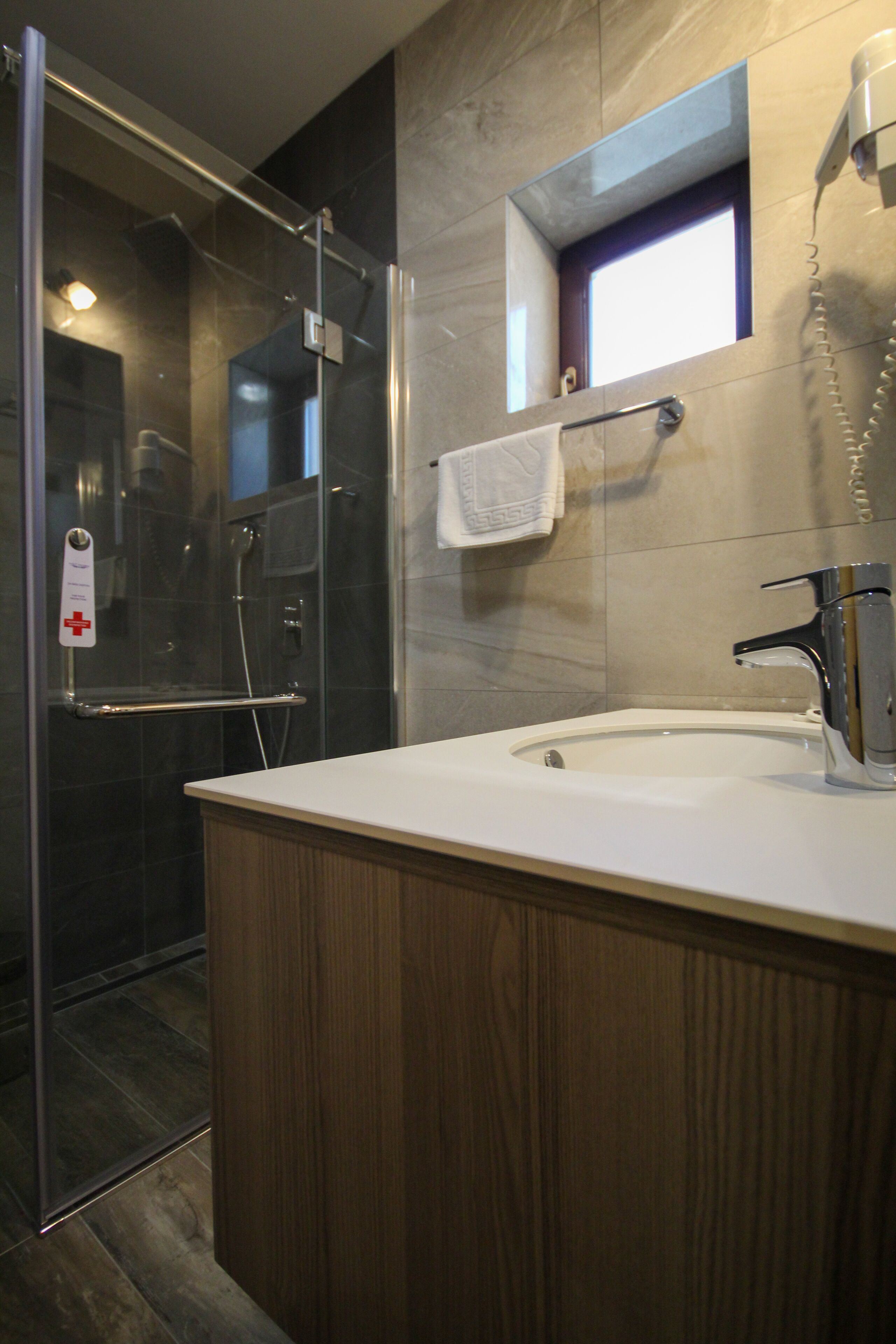 Un baño moderno con cabina de ducha de vidrio, tocador de madera, lavabo con grifo cromado y toallero.