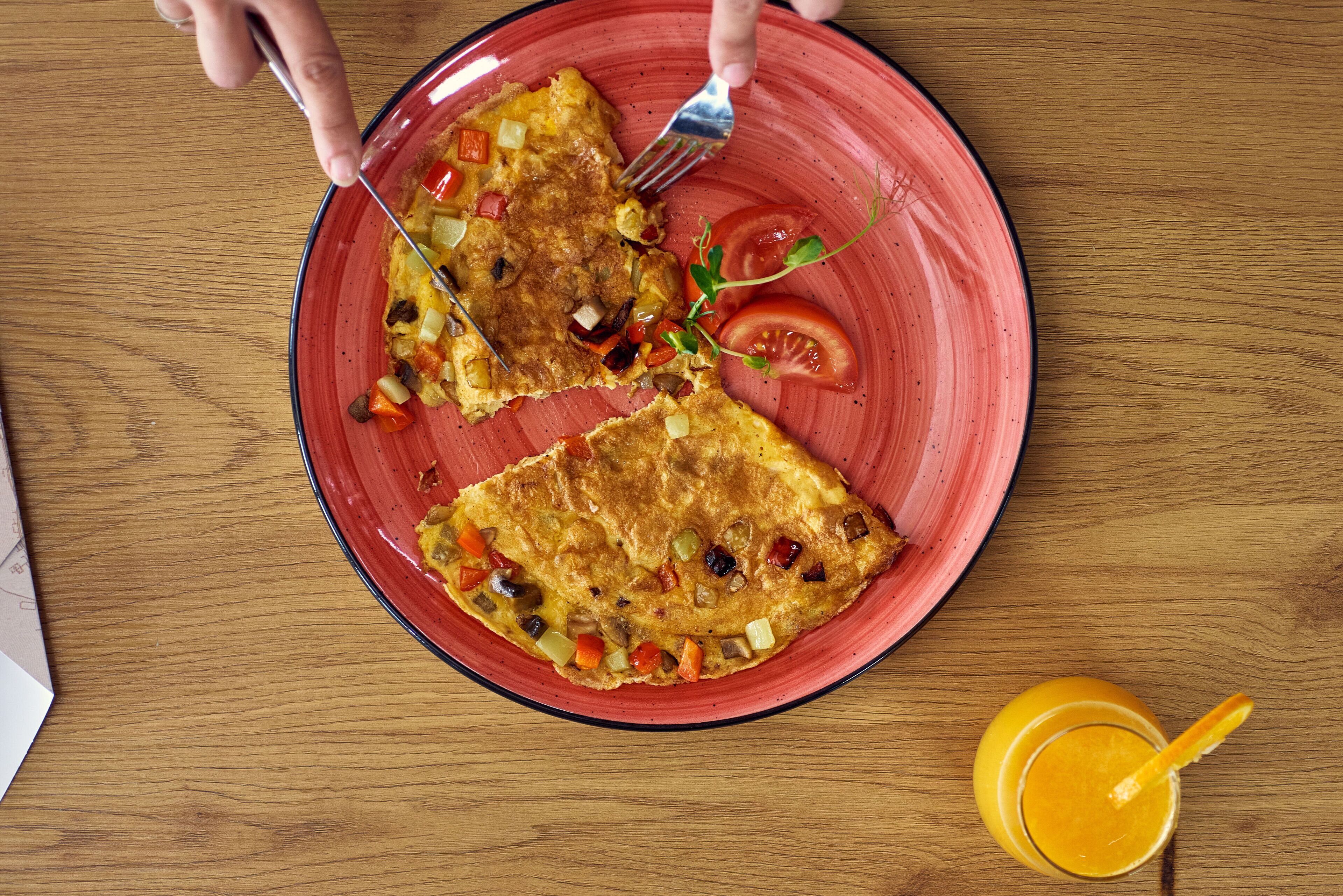 Une assiette avec une part d’omelette et un verre de jus d’orange, posés sur une table en bois.