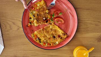 Une assiette avec une part d’omelette et un verre de jus d’orange, posés sur une table en bois.