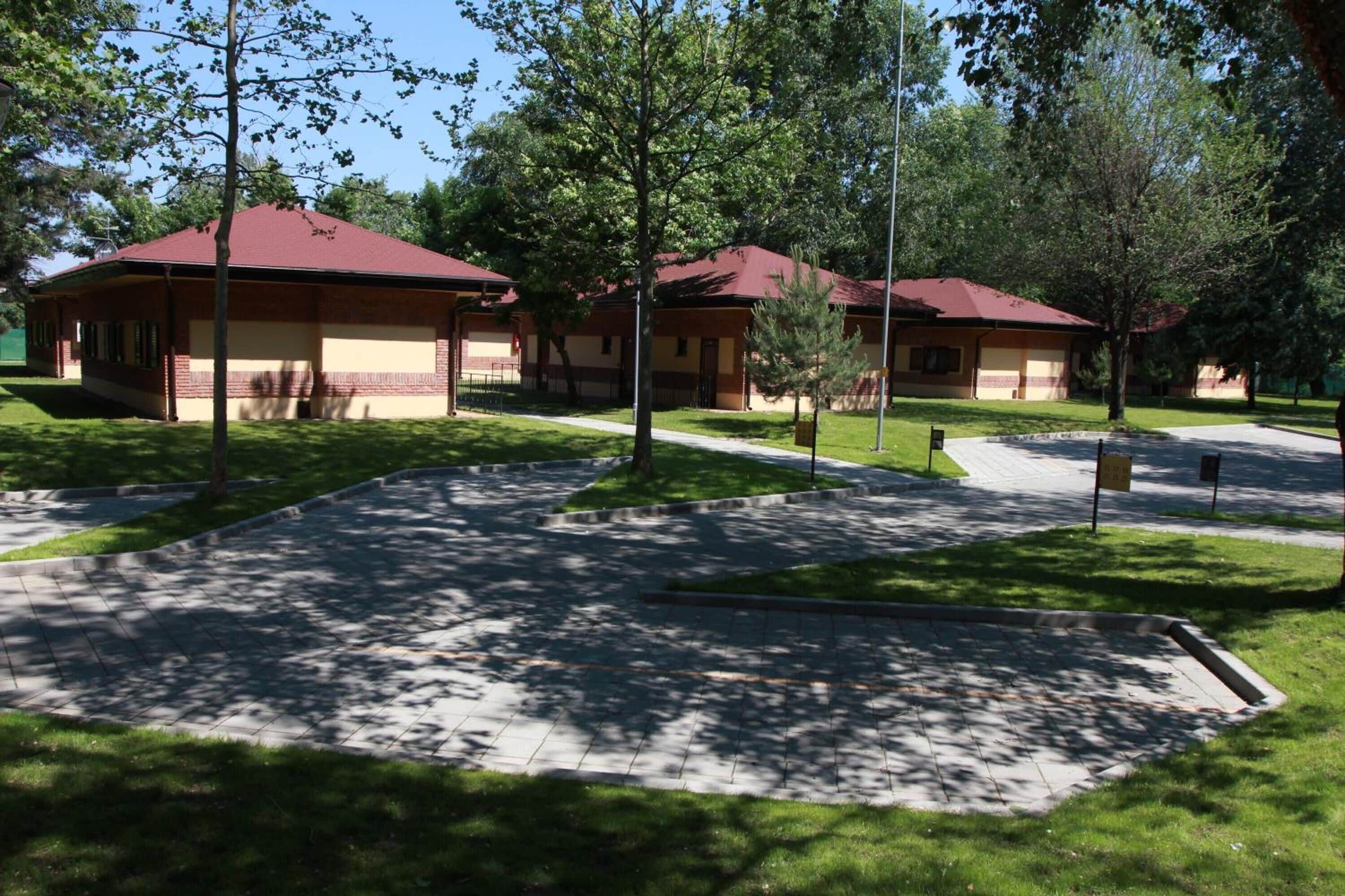 A building with a red roof and beige walls, surrounded by a paved area with trees.