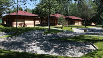 A building with a red roof and beige walls, surrounded by a paved area with trees.