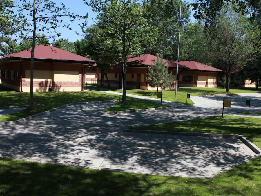 A building with a red roof and beige walls, surrounded by a paved area with trees.