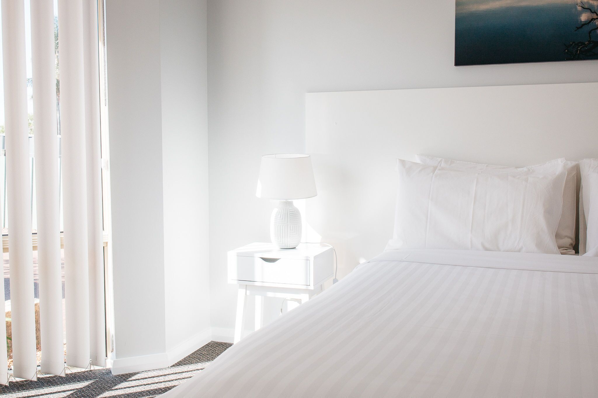 Une chambre d’hôtel avec un grand lit, une table de chevet avec une lampe et une fenêtre avec des rideaux.