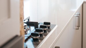 A kitchen with a gas stove, white cabinets, and a brick wall. - Quality Apartments Banksia Albany (Centennial Park)