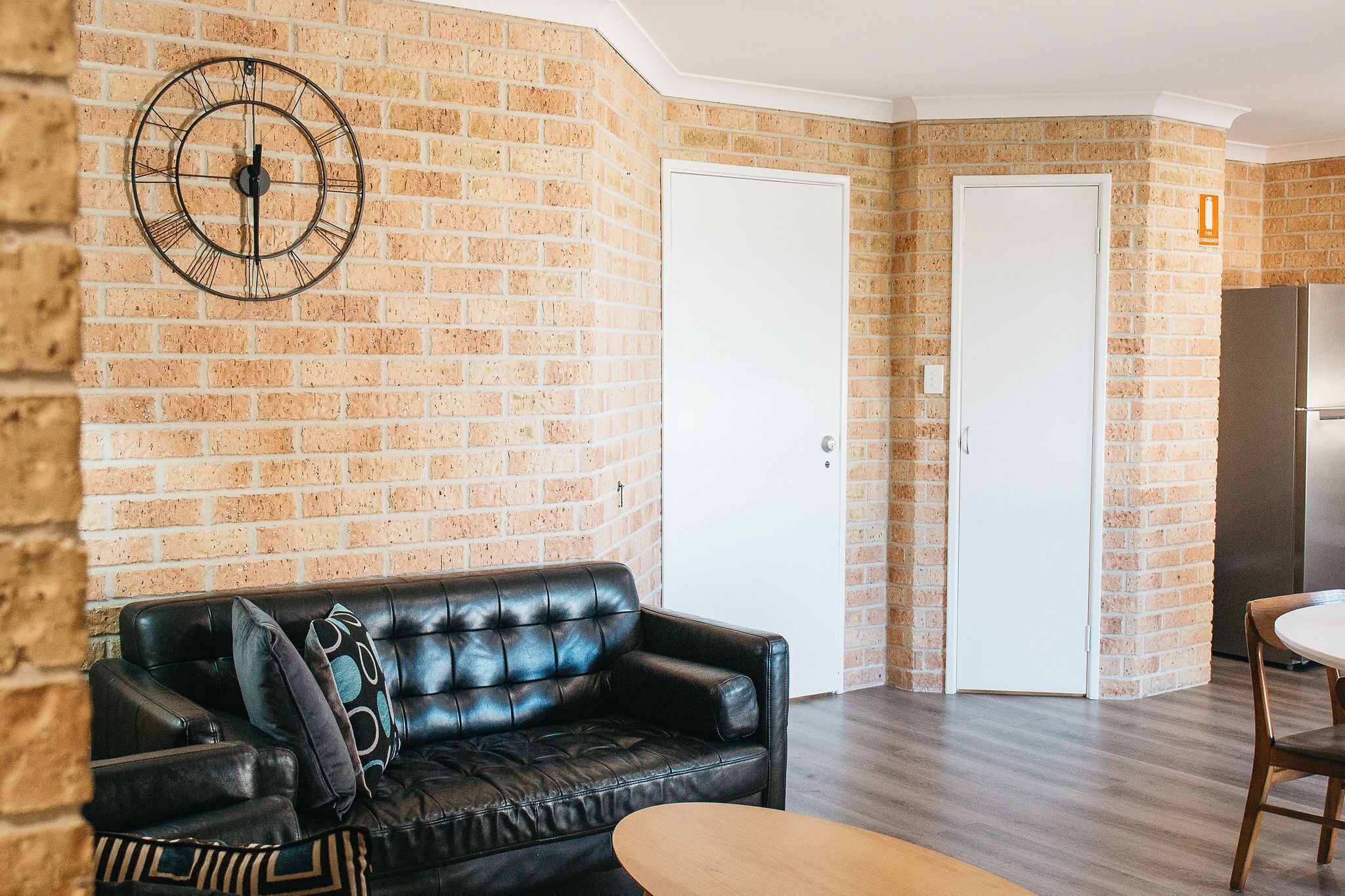 A living room with a brick wall, a black leather sofa, a wooden coffee table, and a white door.