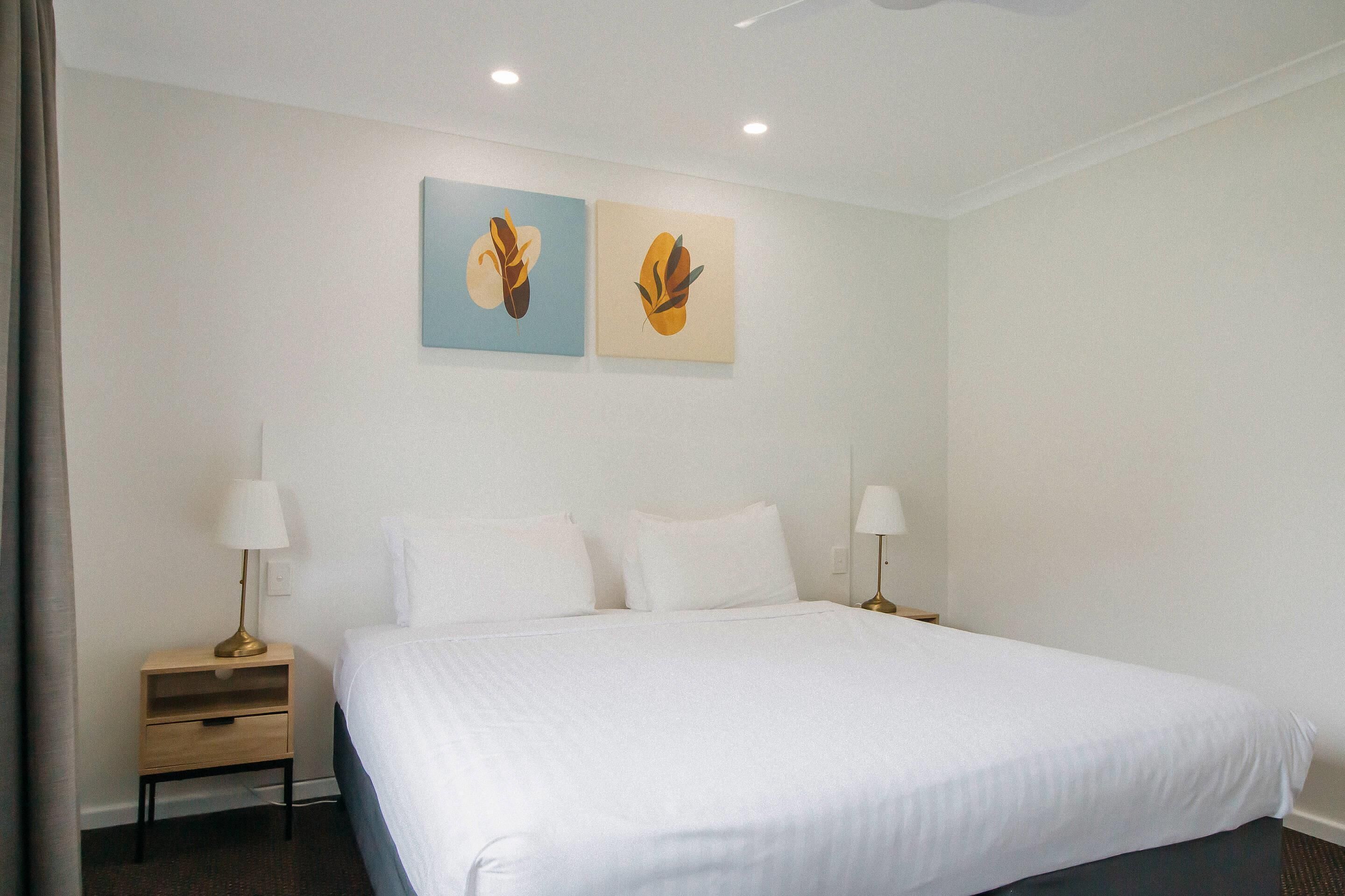 A hotel room with a large bed, two bedside tables with lamps, and two wall-mounted paintings.