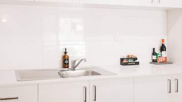 A modern kitchen with white cabinets, a stainless steel sink, and a countertop with various items including a bottle of hand wash soap, a bottle of wine, and a KitKat bar.