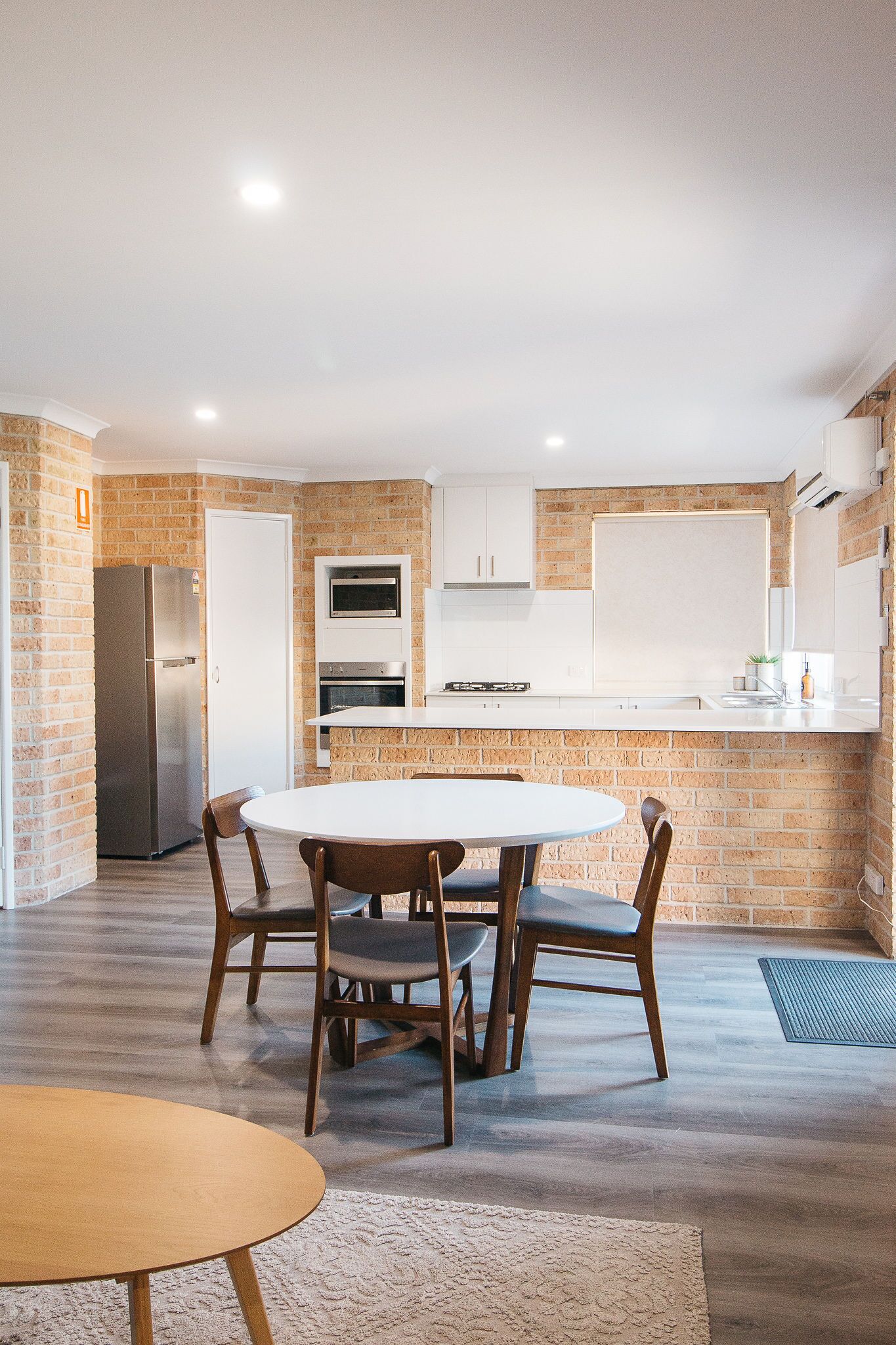 A compact kitchen with a refrigerator, oven, and microwave. There is a dining table with four chairs.