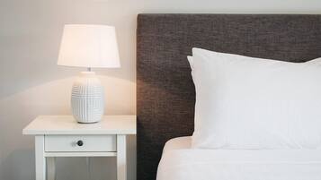 A neatly made bed with white bedding, a white nightstand with a lamp, and a textured headboard.