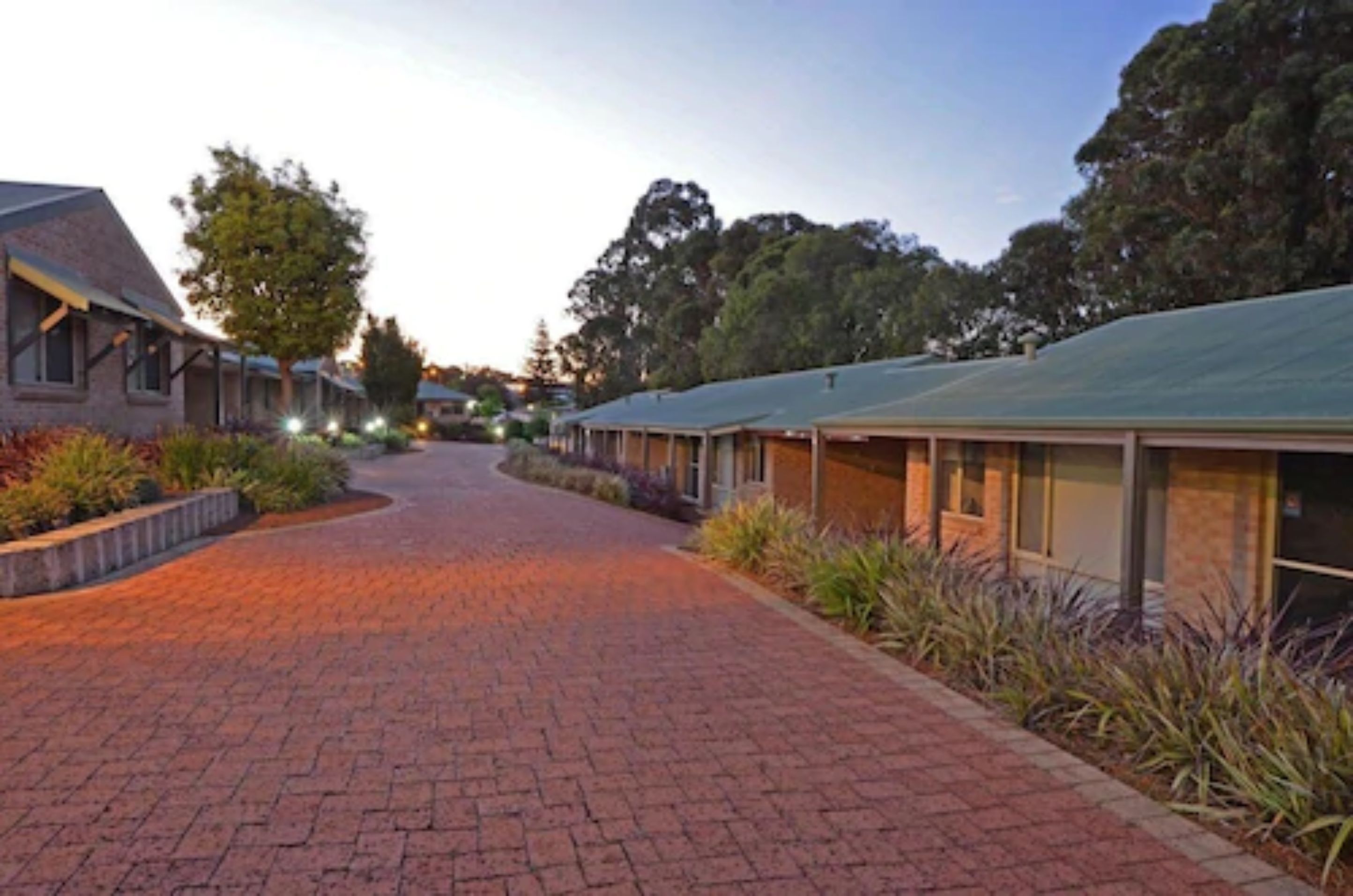 A pathway leading to a row of modern, single-story buildings with large windows, surrounded by landscaped gardens.