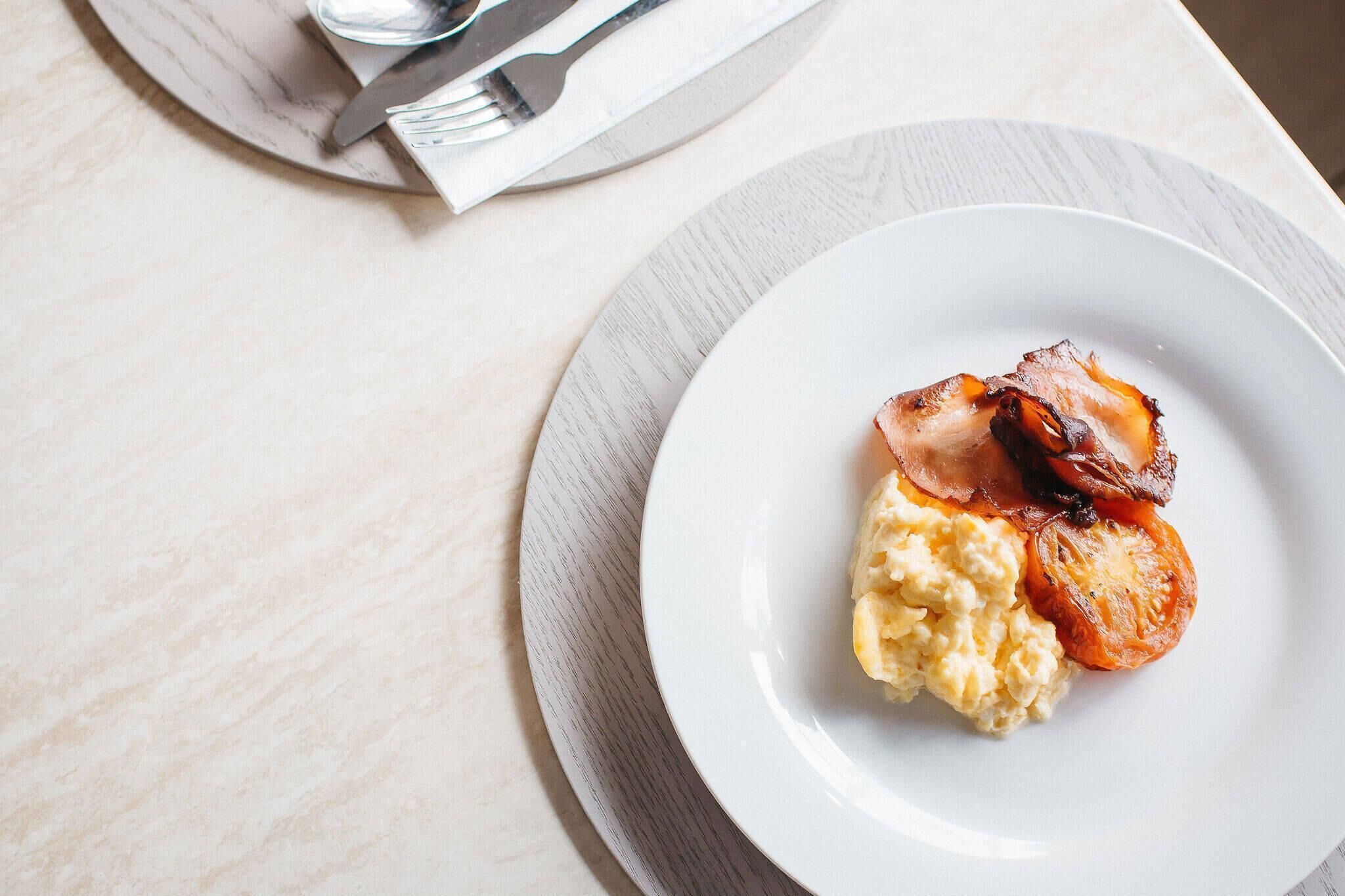 A plate with scrambled eggs and bacon on a white plate.