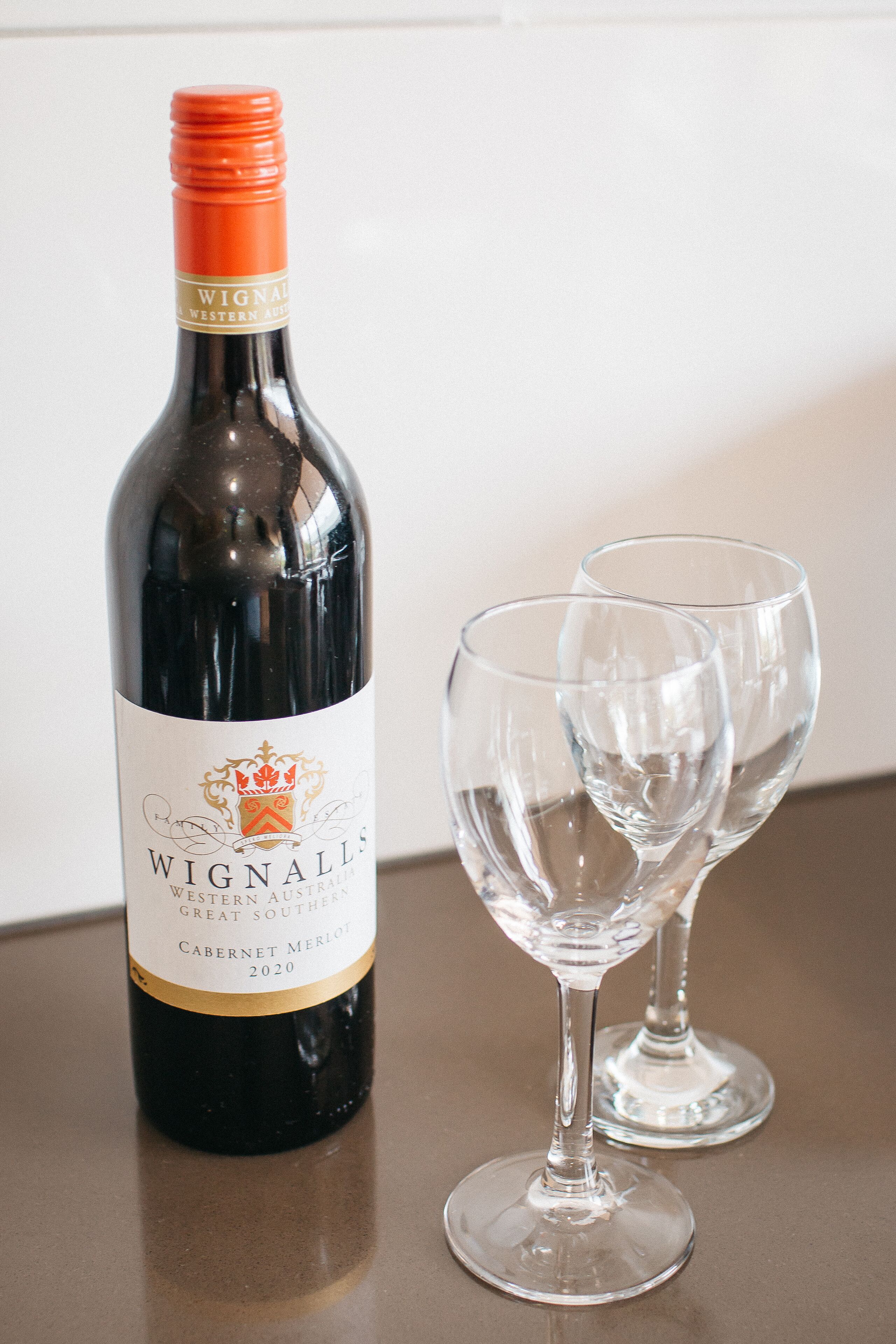 A bottle of Wignall's Cabernet Merlot 2020 next to two empty wine glasses on a table.