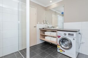 A modern bathroom with a glass shower enclosure, a built-in washing machine, and a large mirror. - Quality Apartments Banksia Albany (Centennial Park)