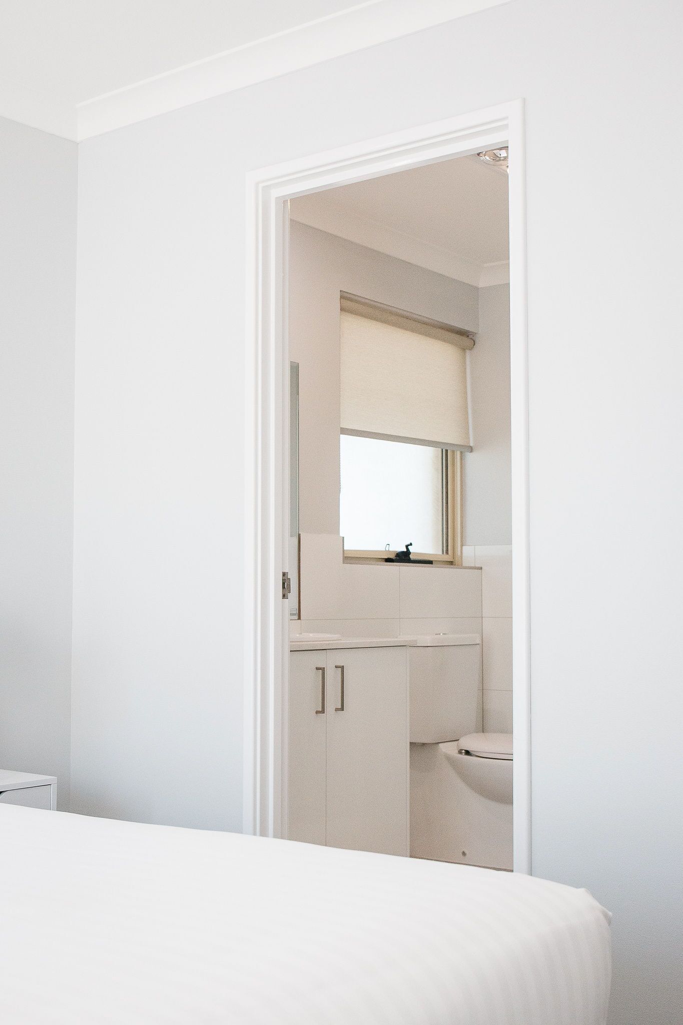 A bedroom with a bed, a white wardrobe, and a bathroom visible through an open door.