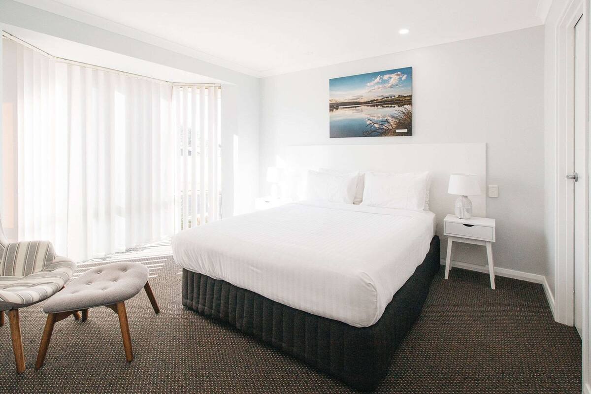 Une chambre d’hôtel avec un grand lit, une chaise, une petite table et un tableau au mur.