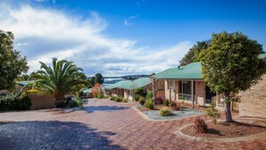 A brick pathway leading to a row of buildings with green roofs, surrounded by trees and shrubs. - Quality Apartments Banksia Albany (Centennial Park)