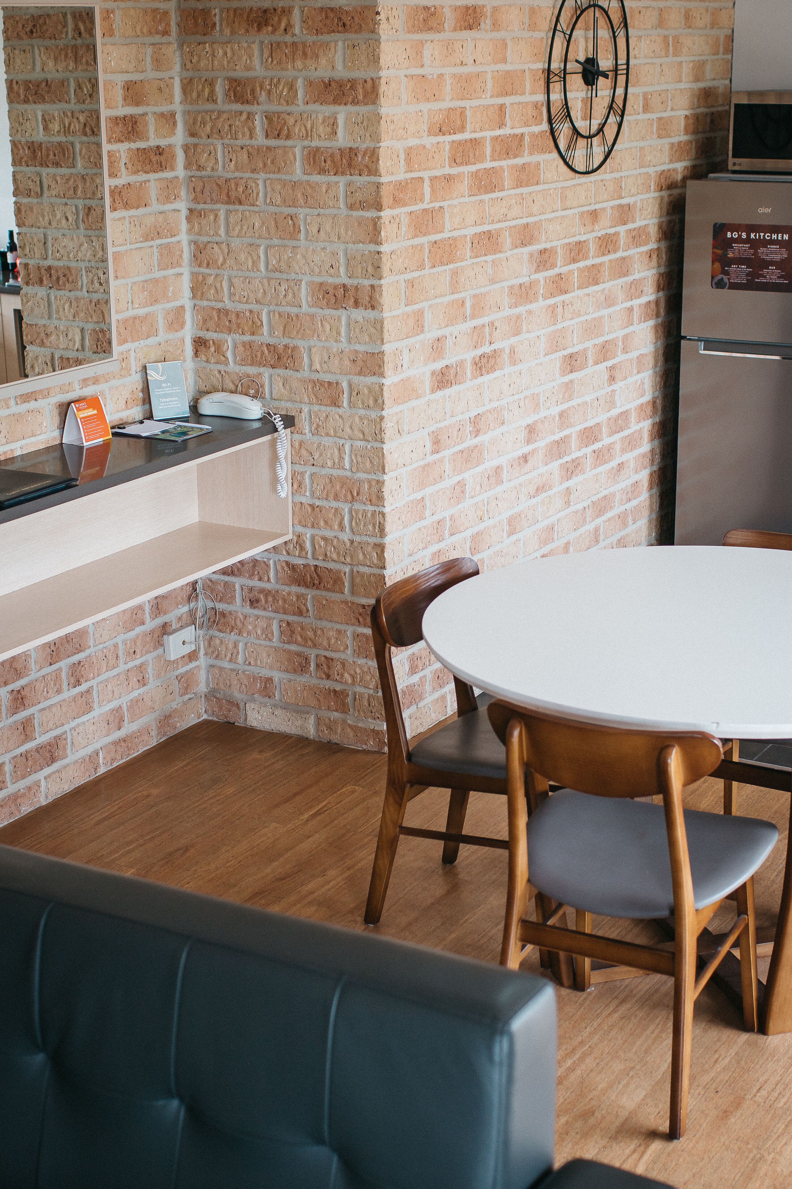 A kitchen with a brick wall, a round table with chairs, a refrigerator, and a wooden bench.