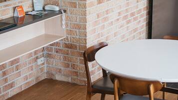A kitchen with a brick wall, a round table with chairs, a refrigerator, and a wooden bench.