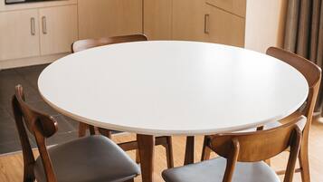 A modern kitchen with a round dining table, wooden chairs, a built-in oven, and a window with curtains.
