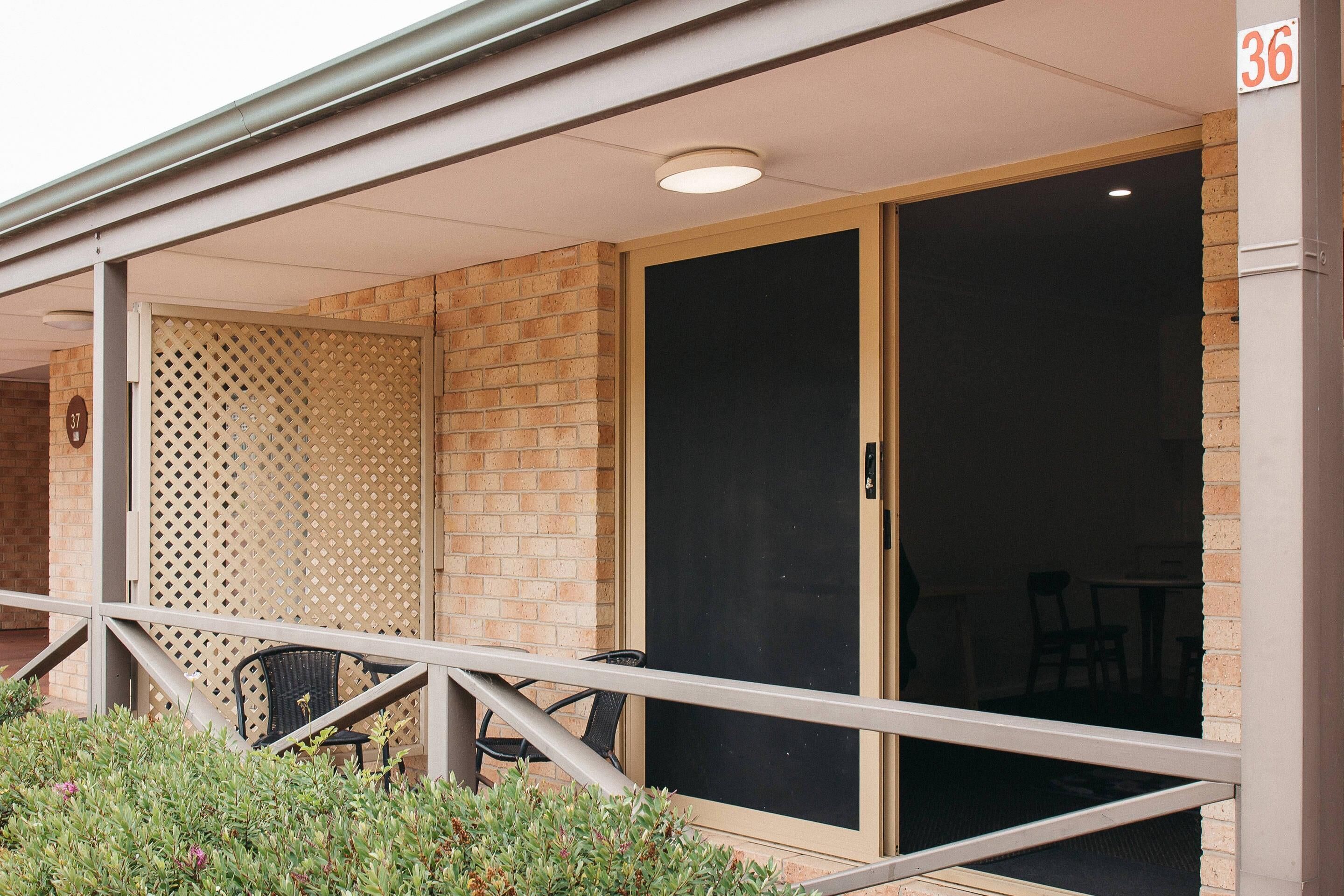 A covered outdoor seating area with a metal railing, a brick wall, and a sliding glass door.