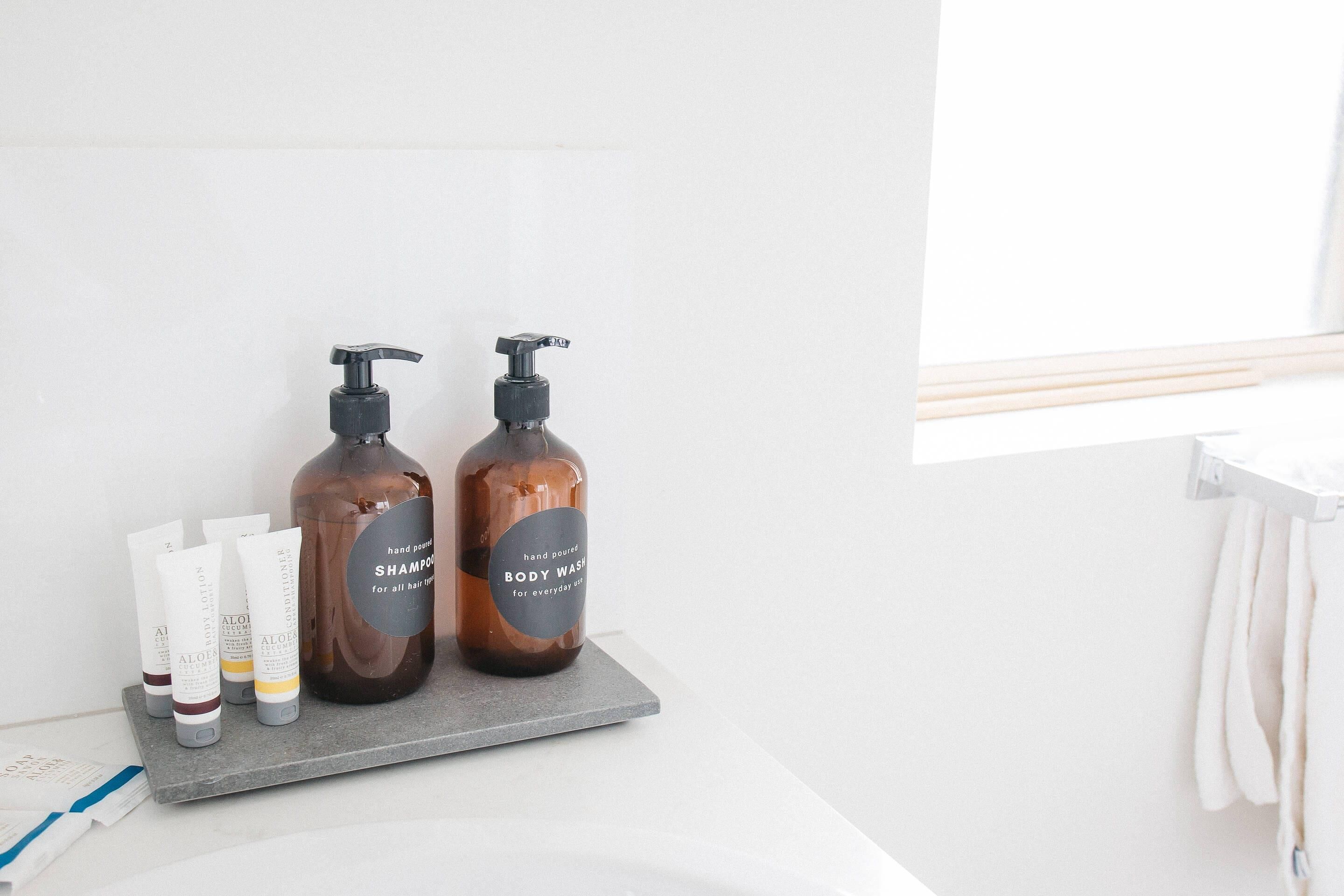 A bathroom with a grey shelf holding various toiletries including shampoo and body wash bottles.