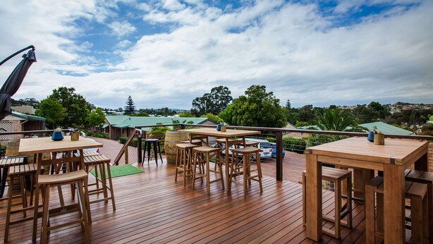 A wooden deck with outdoor seating, including tables and chairs, overlooking a scenic landscape with trees and a distant view of a town. - Quality Apartments Banksia Albany (Centennial Park)