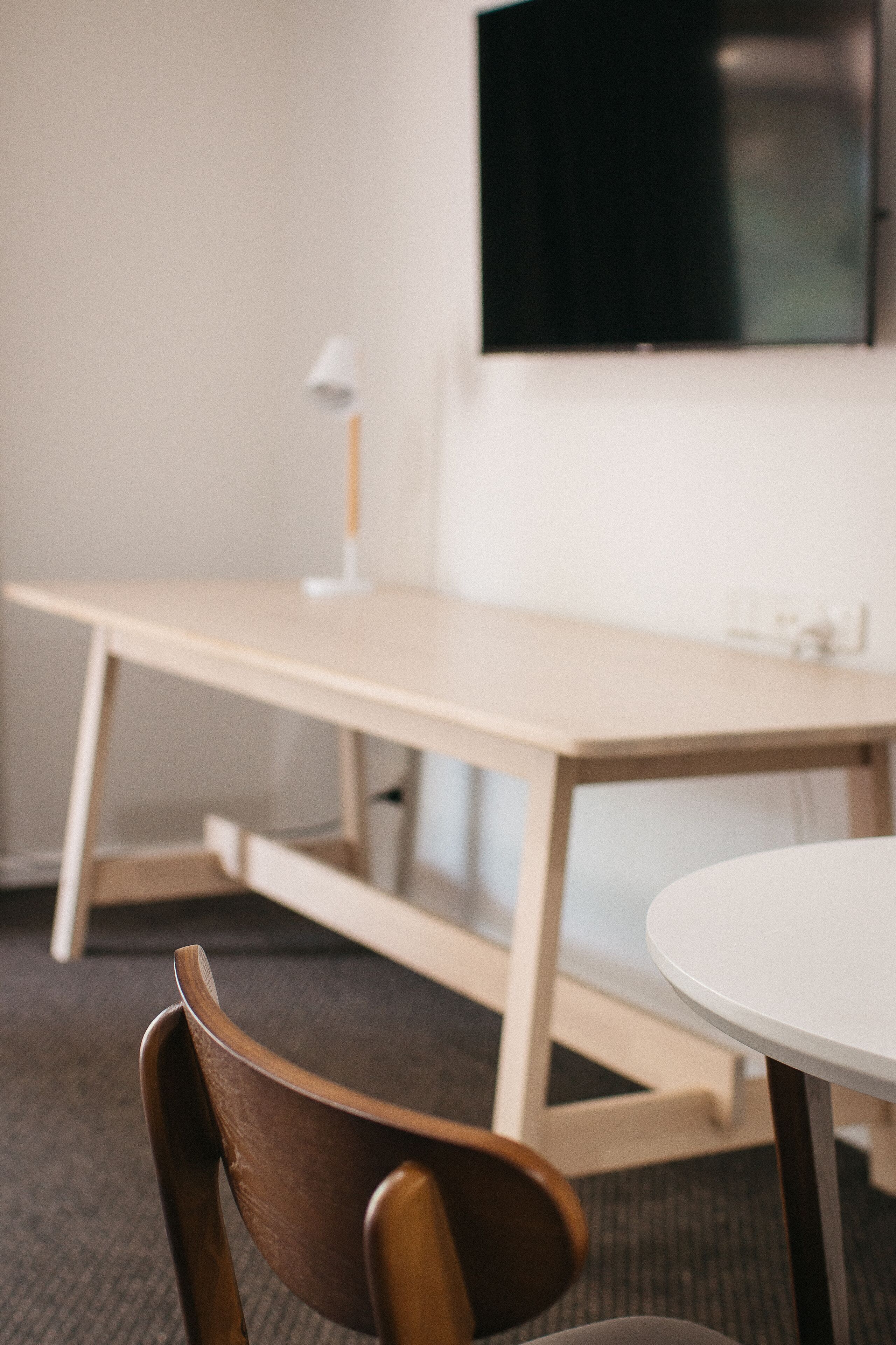 A modern room with a wooden desk, a round table, and a television mounted on the wall.