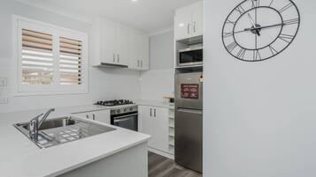 Uma cozinha moderna com armários brancos, uma pia de aço inoxidável, fogão a gás, forno, micro-ondas embutido e geladeira.