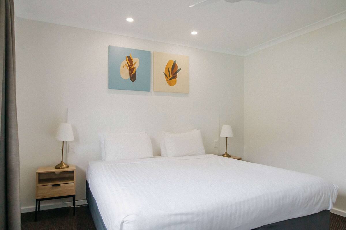 Une chambre d’hôtel avec un grand lit, deux tables de chevet avec des lampes et deux œuvres d’art accrochées au mur.