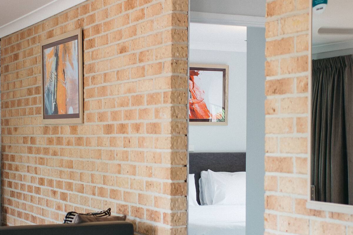 Une chambre d’hôtel moderne avec un mur en briques, un lit, un canapé de couleur sombre et une petite table.