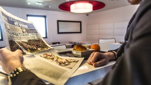A person reading a newspaper in a modern room with a white and red color scheme, a framed picture on the wall, and a bowl of food on the table. - Holiday Inn Express Dijon by IHG (Saint-Apollinaire)