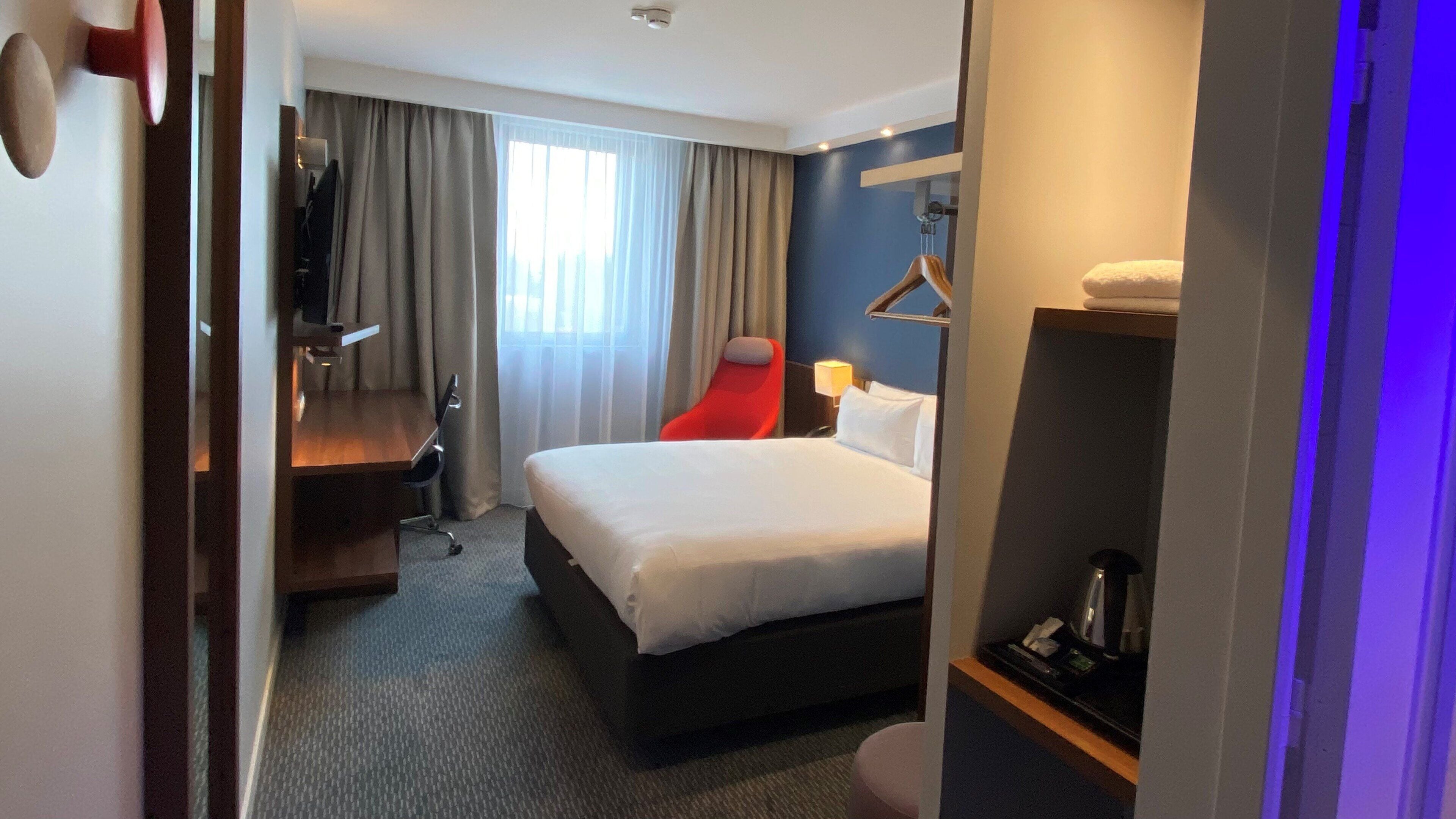 A hotel room with a bed, a desk, a chair, a TV, and a bathroom.