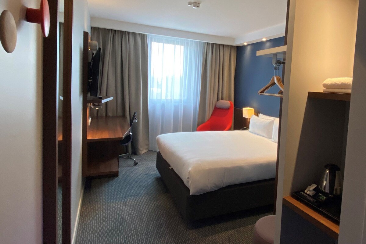 Una habitación de hotel con cama, escritorio, silla, televisor y baño.
