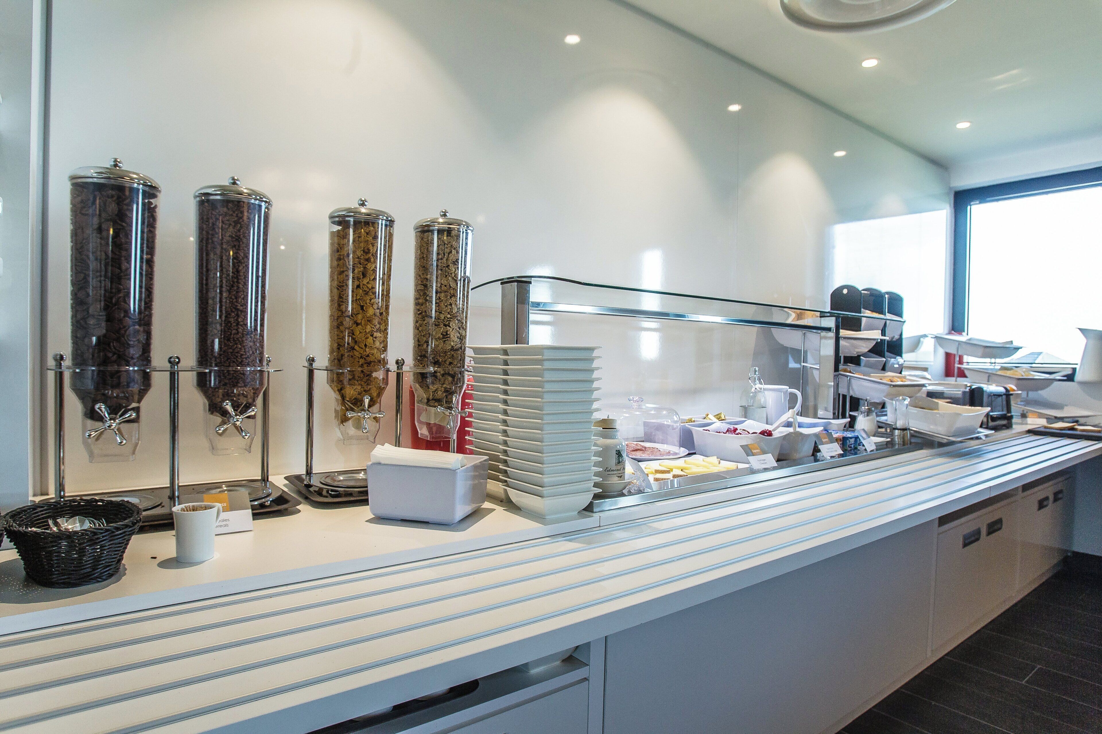 Montaje de bufé con dispensadores de café, diversos alimentos y un separador de vidrio.