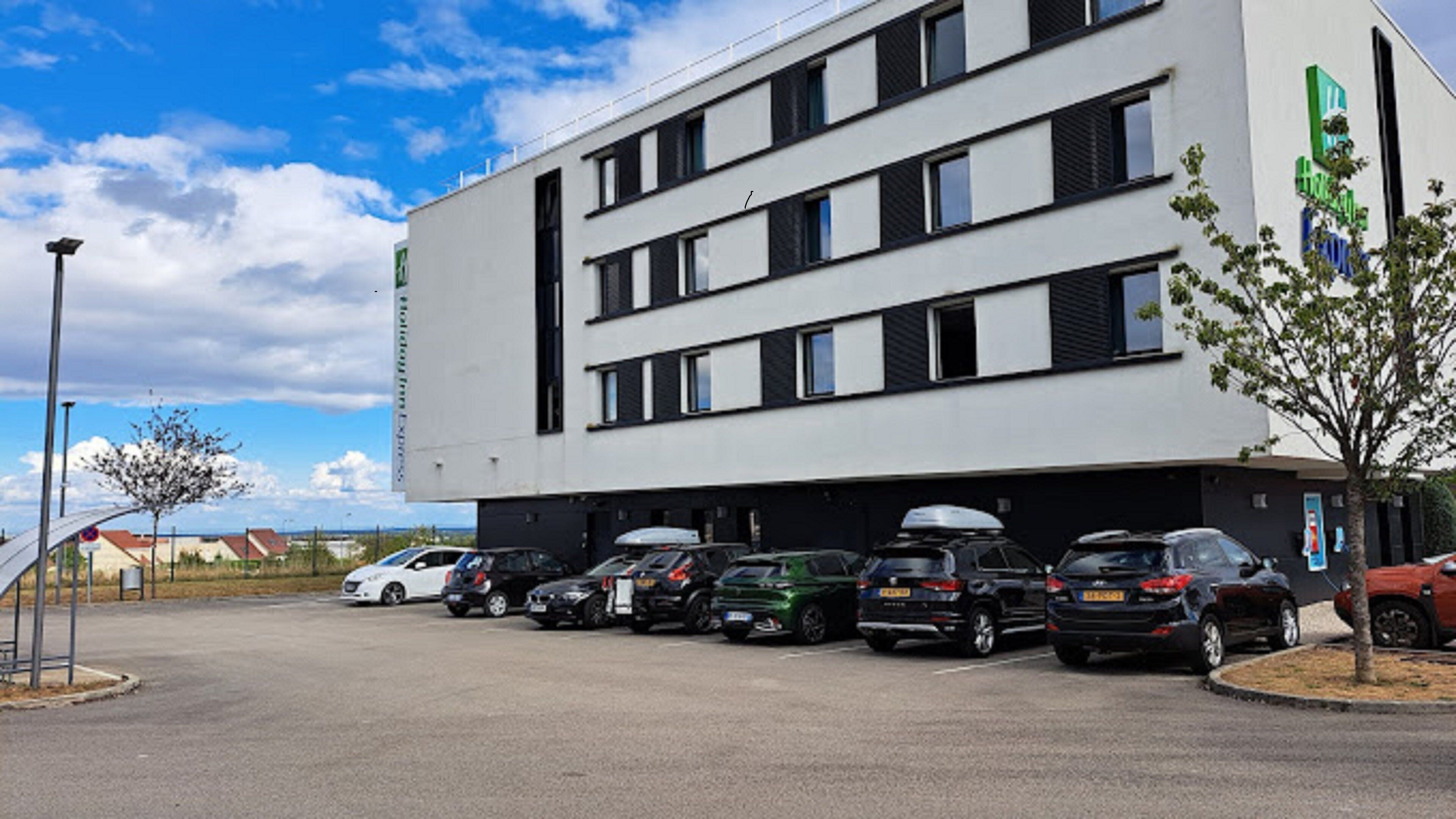A modern building with multiple parking spaces and a row of parked cars.