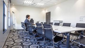 Un salón de conferencias con una mesa blanca, sillas negras y una alfombra estampada.