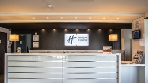 A reception desk with a sign for Holiday Inn Express, a modern design with a dark wall and recessed lighting. - Holiday Inn Express Dijon by IHG (Saint-Apollinaire)