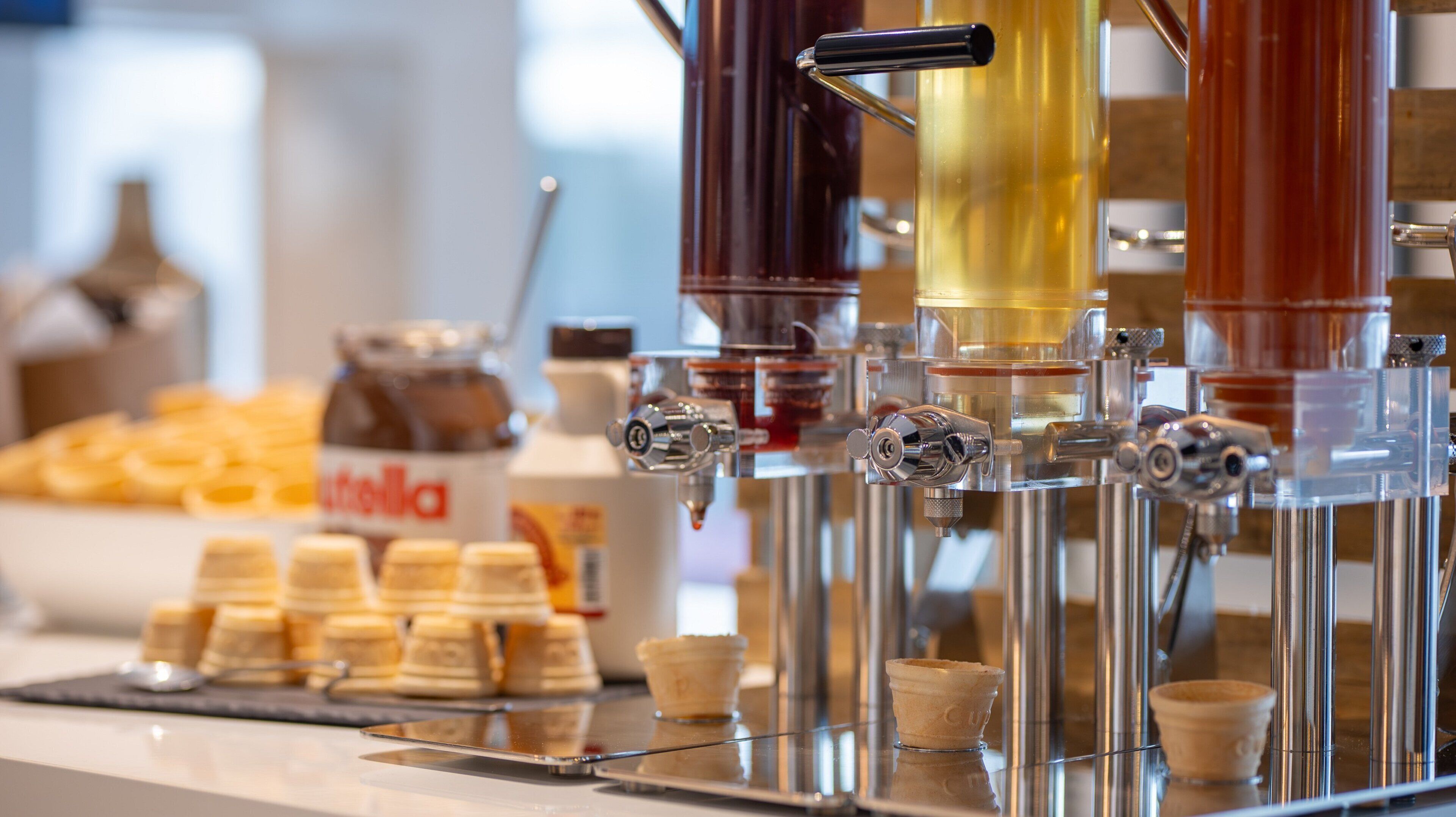 A coffee machine with multiple dispensers, a jar of Nutella, and several cups on a tray.